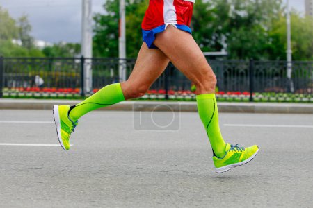 Foto de Primer plano piernas corredor atleta corriendo maratón en la ciudad en calcetines de compresión verde en los pies, deportes carrera de verano - Imagen libre de derechos