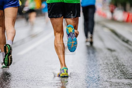 Foto de Piernas atleta corredor masculino carrera maratón en asfalto mojado, gotas de agua en zapatillas de running suela - Imagen libre de derechos