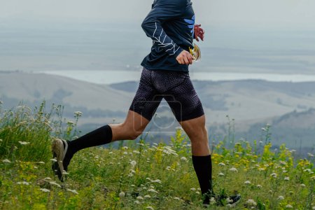Téléchargez les photos : Piste de course de coureur masculin dans l'herbe verte en bas de la montagne, course de marathon d'été - en image libre de droit