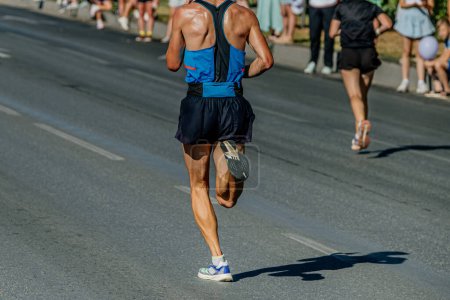 Photo for Rear view male runner running city marathon, hot weather sweat on his back - Royalty Free Image