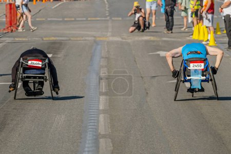 Photo for Two wheelchair racers they go together at marathon race, city summer athletics sports games - Royalty Free Image