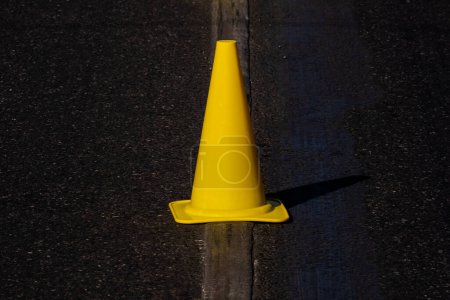 Téléchargez les photos : Cône de circulation jaune debout sur la ligne de marquage routier sur l'asphalte foncé - en image libre de droit