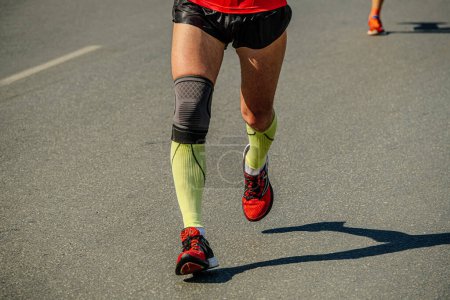 Foto de Close-up piernas corredor masculino en calcetines de compresión y rodilleras correr carrera maratón, deportes juegos de verano - Imagen libre de derechos