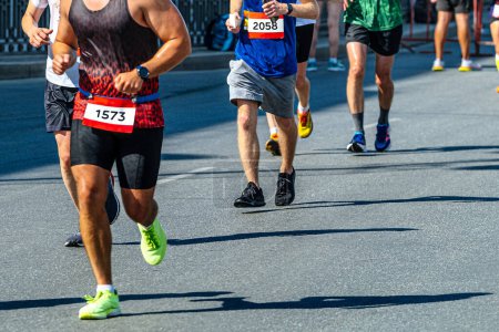 Téléchargez les photos : Vue de côté groupe coureurs masculins courir ensemble en ligne marathon course, ombres sur asphalte gris - en image libre de droit