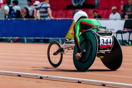 Téléchargez les photos : Homme athlète en fauteuil roulant stade de course sur piste dans le championnat de para athlétisme, sur sa tête est casque blanc - en image libre de droit