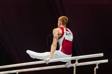 Photo for Gymnast exercise parallel bars in championship gymnastics, element l-sit in support or through support on 2 bars - Royalty Free Image