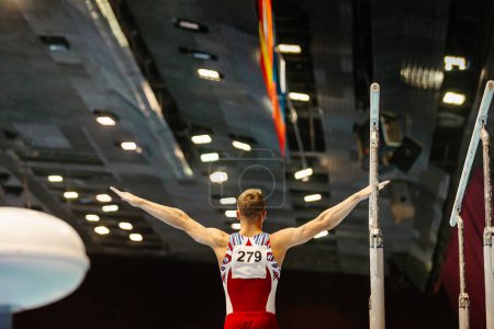 Foto de Gimnasta vista trasera ejercicio de inicio barras paralelas en la gimnasia de campeonato - Imagen libre de derechos