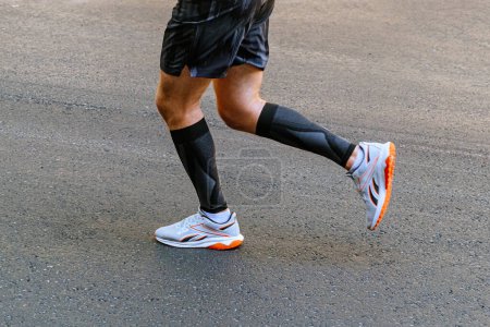 Foto de Piernas corredor masculino en mangas de compresión negro corriendo en carrera de maratón de asfalto carretera - Imagen libre de derechos