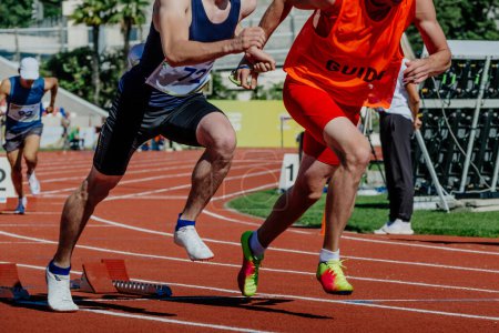 Photo for Blind para athlete runner with guide in starting blocks running race, summer para athletics championships - Royalty Free Image