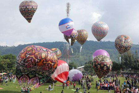 Téléchargez les photos : Karanganyar, Indonésie - 20 novembre 2022. Festival des montgolfières. ballons géants colorés. Les gens célèbrent avec enthousiasme le festival. foule. sur un terrain de soccer avec vue sur la colline. - en image libre de droit