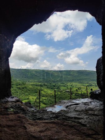 The image captures a breathtaking view from a cave opening, where the sky and the lush green landscape meet, creating a serene and picturesque scene.