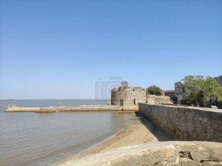 The image shows a serene coastal scene with a Diu Fortress and a body of water presumably a lake.