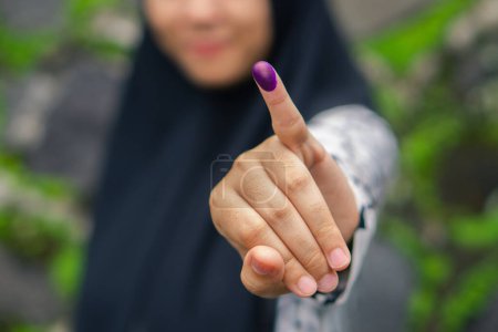 Blurry half face muslim girl showing pinky finger after voting on Indonesia presidential election. Election ads concept.