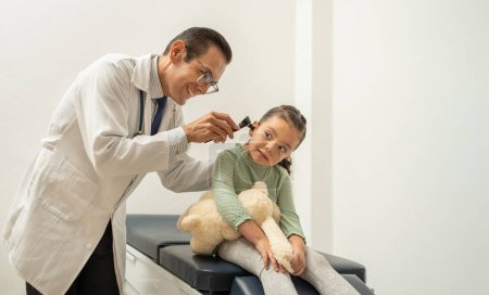 Photo for Smiling hispanic pediatrician examining kid ear with otoscope, child at doctor's office. Latin doctor checking girl ear using an auroscoper. - Royalty Free Image