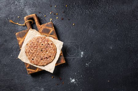Raw burger patty on a wooden board and on a black background. Top view. Space for text.