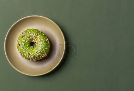 Apetitivo, donut pistacho en un plato y sobre un fondo de color. Colocación plana, con espacio para texto.