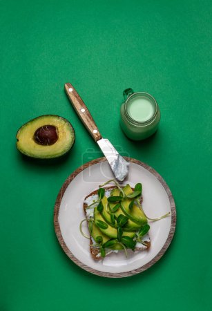 Bread toast on a white plate with avocado slices and micro greens. Top view, flat lay.