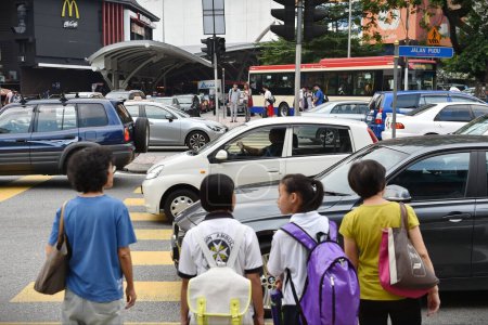Foto de Kuala Lumpur, 19 de junio de 2015: El tráfico se mueve lentamente a lo largo de una concurrida carretera del centro de la ciudad mientras los peatones esperan para usar un cruce de cebra. - Imagen libre de derechos