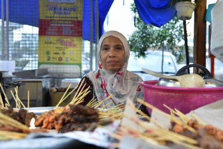 Téléchargez les photos : Une femme vend du satay et d'autres aliments à un marché de rue le 19 juin 2015 à Kuala Lumpur, en Malaisie. La capitale malaisienne est célèbre pour sa cuisine de rue et fusion asiatique. - en image libre de droit