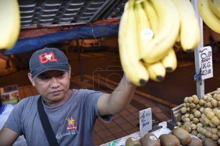 Photo for A street market trader sells bananas and other fruits on June 19, 2015 in Kuala Lumpur, Malaysia. The Malaysian capital is famous for its street markets and foods. - Royalty Free Image