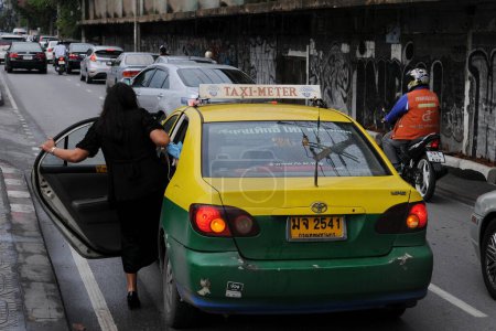 Foto de Una mujer se sube a un taxi en una concurrida calle del centro de la ciudad el 16 de agosto de 2011 en Bangkok, Tailandia. Los taxis registrados son ubicuos en toda la capital tailandesa, con aplicaciones de uso compartido cada vez más comunes. - Imagen libre de derechos