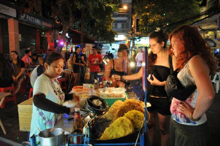 Foto de Un vendedor ambulante sirve fideos a los clientes en Khao San Road el 30 de junio de 2013 en Bangkok, Tailandia. La capital tailandesa es famosa por la variada y deliciosa comida callejera popular entre los lugareños y turistas. - Imagen libre de derechos