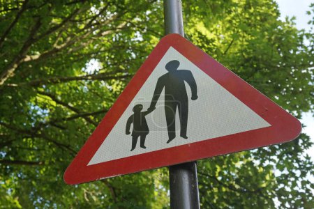 View of a generic road sign depicting a child holding the hand of an adult advising motorist to expect pedestrians on the road ahead