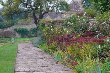 Photo for Scenic summertime view of a stone paved path through a beautiful English style landscape garden with a flowers in bloom and green leafy plants - Royalty Free Image