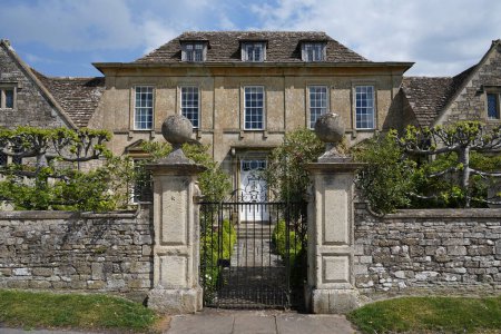 Photo for Exterior view of surrounding stone wall and ornate gateway of a beautiful old mansion house on a street in an English village - Royalty Free Image