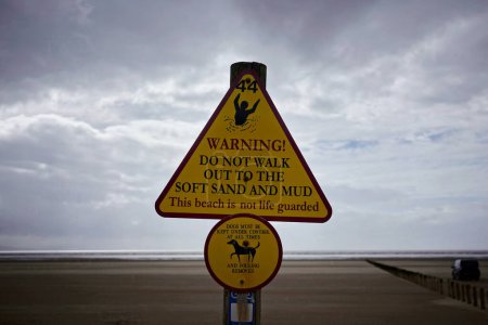 Téléchargez les photos : Vue des panneaux d'avertissement génériques sur une plage avec un ciel orageux au-dessus - le panneau met en garde contre les sables mouvants - en image libre de droit