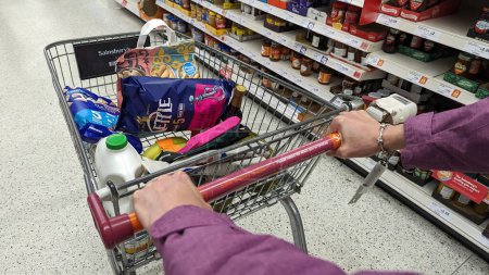 Photo for A trolley full of food products is pushed along a Sainsburys supermarket aisle on October 19, 2023 in London, UK. Sainsburys is Britain's 2nd largest supermarket retailer after Tesco with 1400 stores. - Royalty Free Image