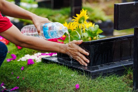 Foto de Mujer limpiando lápidas mientras visita a familiares fallecidos usando agua embotellada en un día soleado - Imagen libre de derechos