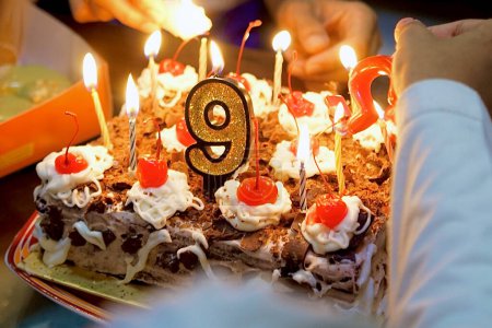 La célébration du gâteau d'anniversaire de 9e année faite maison avec une grande bougie numérique et de nombreuses petites bougies illuminent l'ambiance. Deux personnes allument les bougies. Vue du côté supérieur