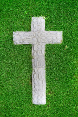 White cross christian sign made from natural stone and white coat on a green grass during hot sunny day.
