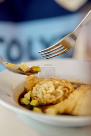 Una persona que come una porción de Pempek de plato indonesio que contiene Kapal Selam y Keriting. Un par de corte de pepino y sabroso condimento picante delicioso pempek vertido en el tazón.