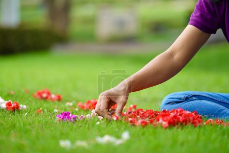 Une personne sème des pétales de fleurs rouges, blanches et violettes sur l'herbe verte (également connue sous le nom de Nyekar dans la culture javanaise / indonésienne).