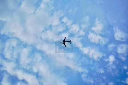 Ein Flugzeug, das in unmittelbarer Nähe über dem Kopf fliegt. Der Himmel ist blau. Die Wolke ist weiß mit sehr klarem Himmel. Die Flugrichtung befindet sich links vom Rahmen.