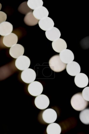 A light bokeh in diagonal orientation. Painted in front of dark background, the light traces are dominated with white, gold, and warm color.
