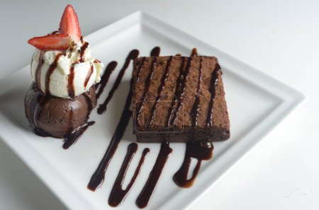 Schokoladenbrownie serviert mit Schokolade und Vanilleeis, Schokoladensauce und Erdbeergarnitur.