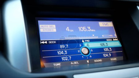 A large blue liquid crystal screen of the multimedia head unit on the central console of the car, with radio control buttons