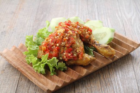 Foto de Ayam penyet es un plato de pollo frito indonesio que consiste en pollo frito que se rompe con el mortero contra el mortero para hacerlo más suave, servido con sambal, rodajas de pepinos, tofu frito y tempeh. - Imagen libre de derechos