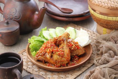 Photo for Ayam penyet  is Indonesian fried chicken dish consisting of fried chicken that is smashed with the pestle against mortar to make it softer, served with sambal, slices of cucumbers, fried tofu and tempeh. - Royalty Free Image
