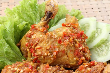 Foto de Ayam penyet es un plato de pollo frito indonesio que consiste en pollo frito que se rompe con el mortero contra el mortero para hacerlo más suave, servido con sambal, rodajas de pepinos, tofu frito y tempeh. - Imagen libre de derechos