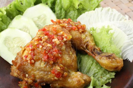 Photo for Ayam penyet  is Indonesian fried chicken dish consisting of fried chicken that is smashed with the pestle against mortar to make it softer, served with sambal, slices of cucumbers, fried tofu and tempeh. - Royalty Free Image