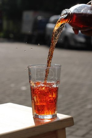 Téléchargez les photos : Pouring cola with ice cubes on a wooden table - en image libre de droit