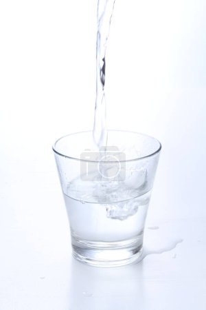 Téléchargez les photos : Verser de l'eau dans un verre de fond blanc - en image libre de droit