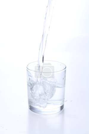 Téléchargez les photos : Verser de l'eau dans du verre sur fond blanc - en image libre de droit