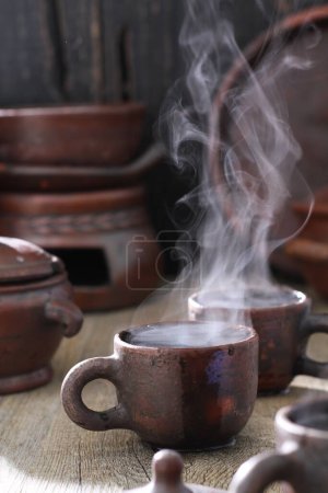 Photo for A closeup shot of a teapot with a cup of tea on a wooden table - Royalty Free Image