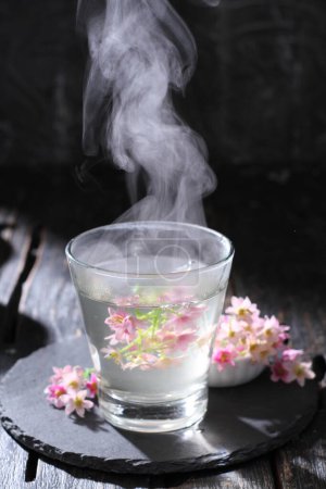Téléchargez les photos : Thé et fleurs dans un verre de lait sur fond noir - en image libre de droit