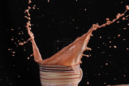 Téléchargez les photos : Éclaboussure de chocolat dans le verre sur un fond brun - en image libre de droit
